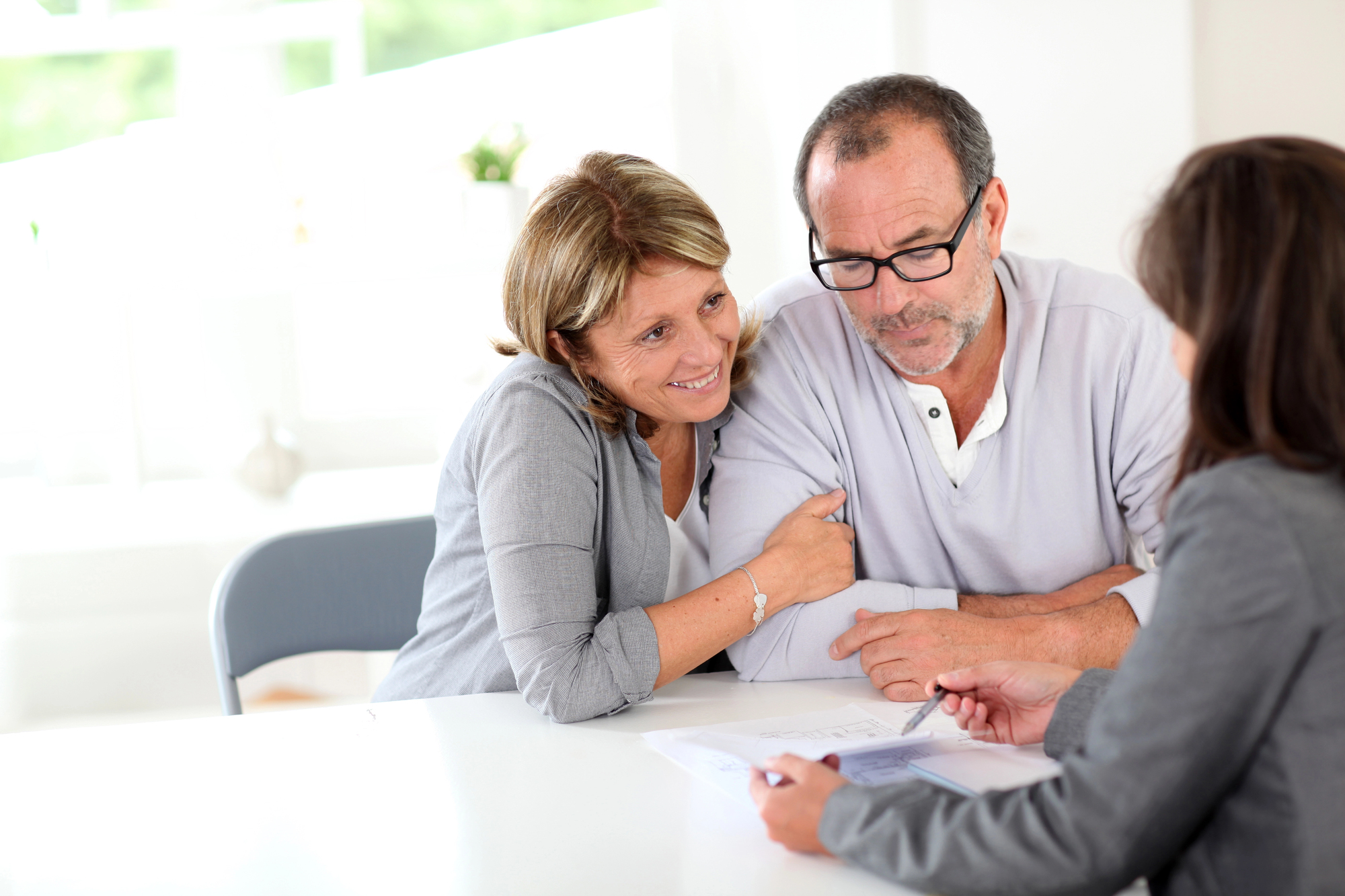 Smiling Couple Having A Professional Consultation With A Designer At A Well-Lit, Modern Office Table.