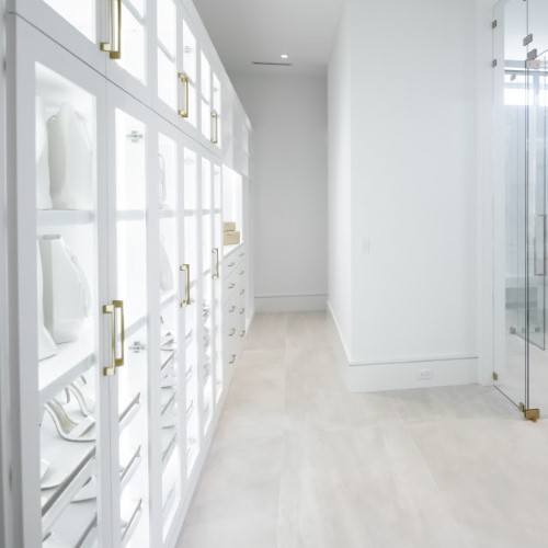 Luxury Walk-In Closet With Glass Cabinets, White Cabinetry, And Gold Hardware, Showcasing Custom Storage Solutions.