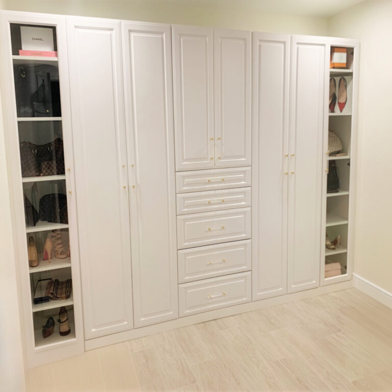 White Reach-In Closet With Glass Door Shelving And Integrated Drawers.