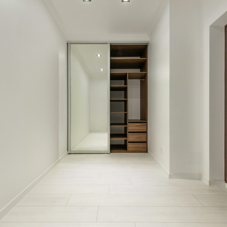Modern Custom Reach In Closet With Mirrored Sliding Doors And Wooden Shelving For Optimized Storage.
