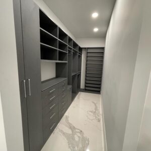 Modern walk-in closet with dark custom cabinetry, open shelving, and hanging space.