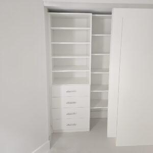 Small reach-in closet with custom shelving and drawers in a minimalist white design.