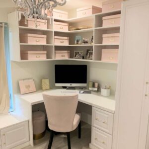 Small home office with built-in desk, white cabinetry, shelving, and pastel storage boxes.