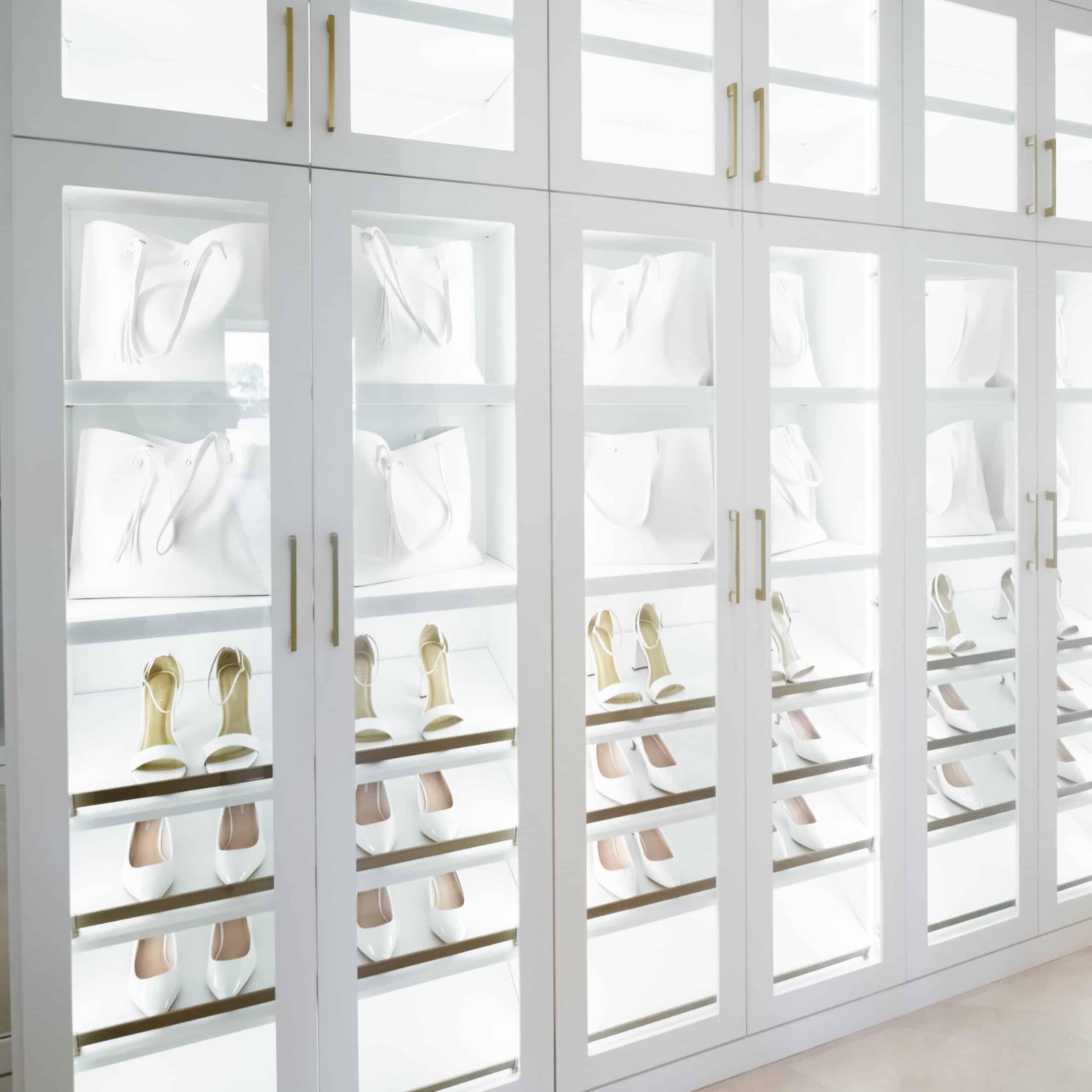 Luxury custom shoe storage closet with illuminated shelves displaying designer handbags and high heels.