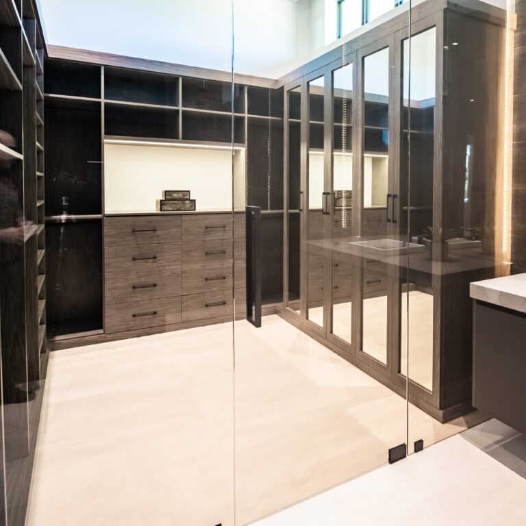 Modern Walk-In Closet With Custom Cabinetry, Glass Doors, Integrated Lighting, And Ample Storage Space.